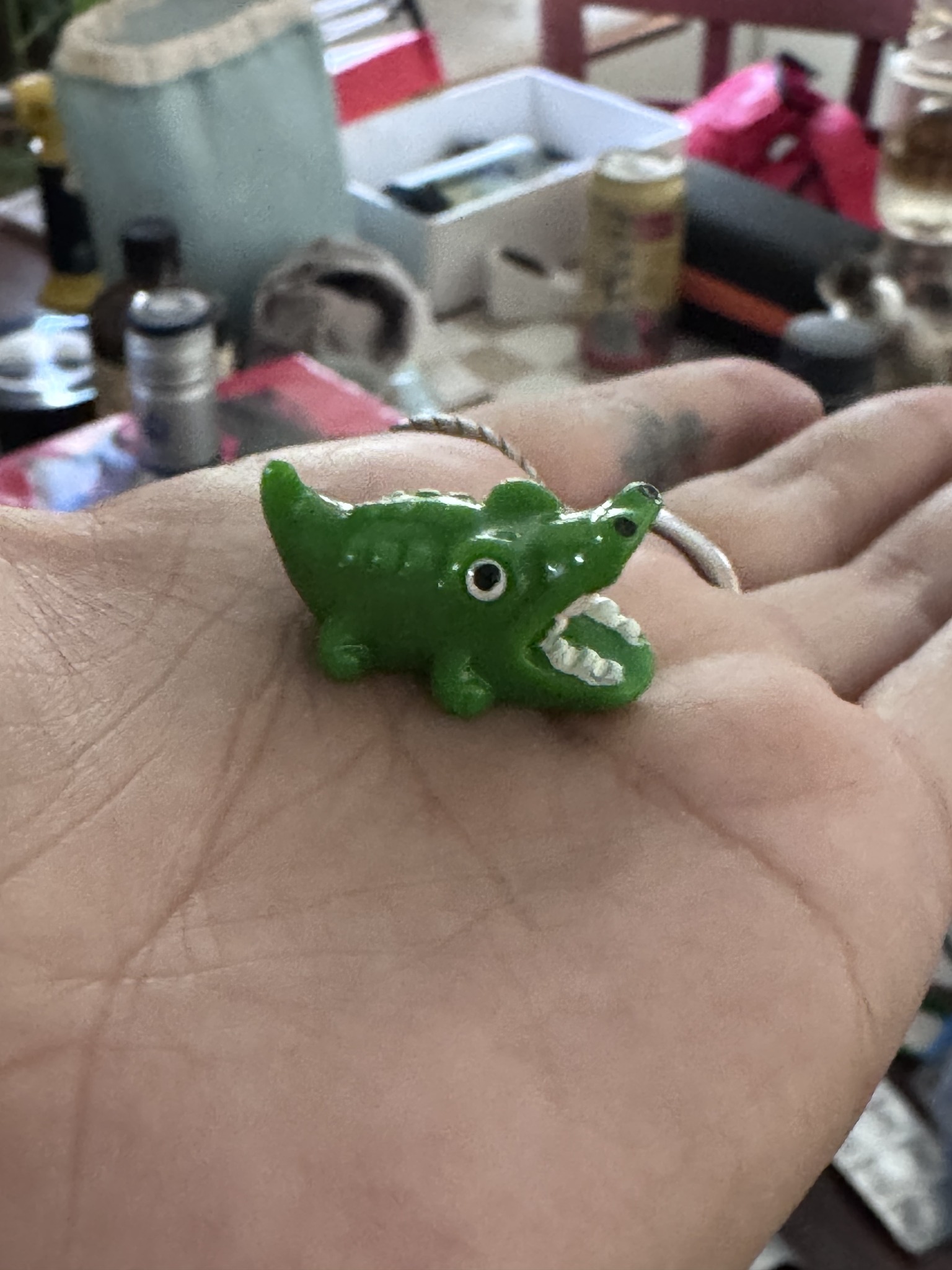 A tiny green alligator figurine with an open mouth resting in Kat’s palm